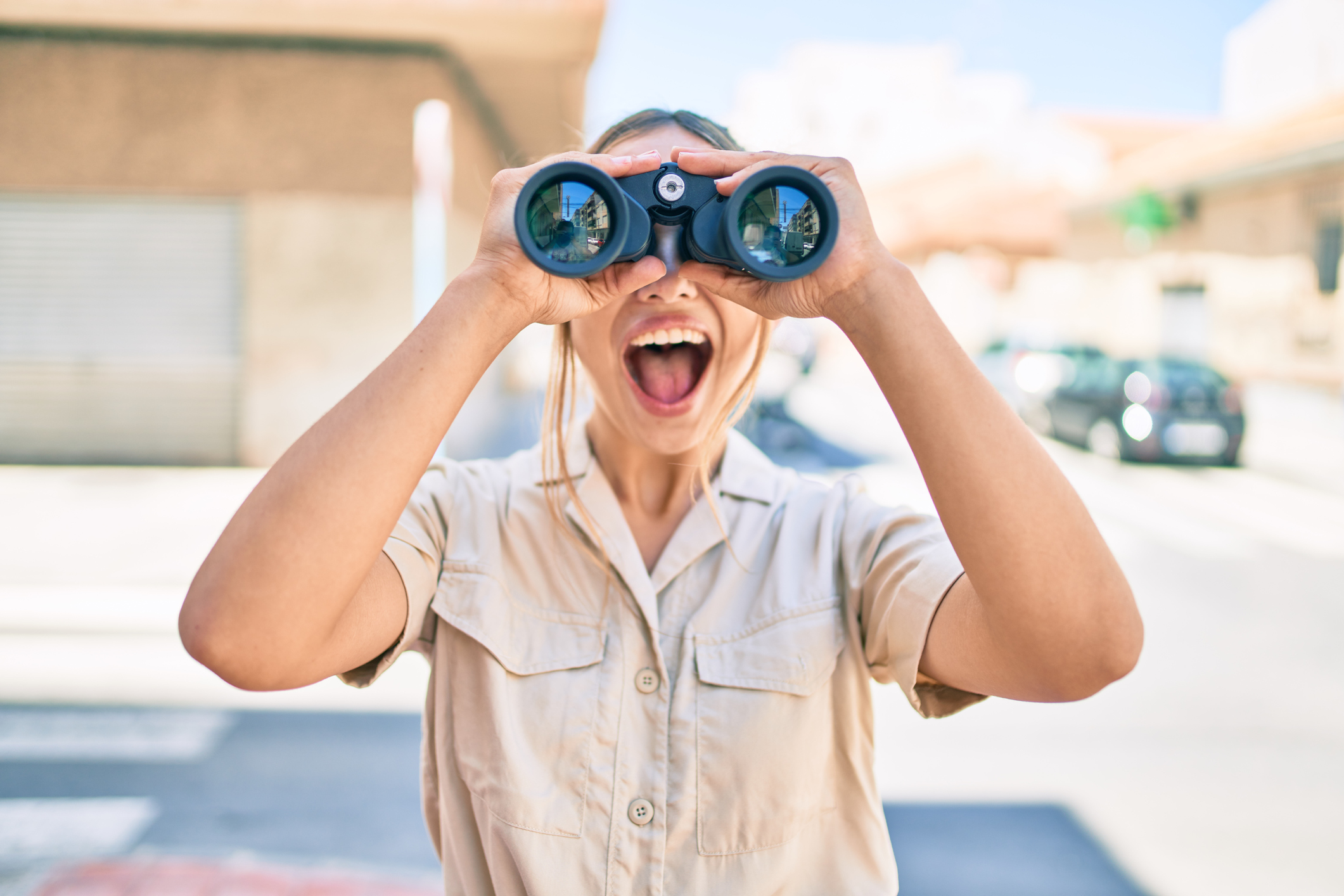 Young beautiful blonde caucasian woman smiling happy outdoors on a sunny day looking through binoculars